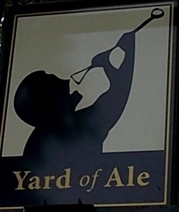 Inn sign. Man in silhouette drinking rom yard of ale (long glass) pointing diagonall upwards to right. Yard of Ale sign Stratford-on-Avon. Image by Jaggery CC BY-SA 2.0 via Wikimedia Commons