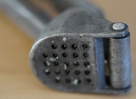 Garlic press with bits of garlic in holes
