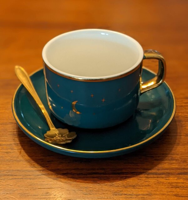 Blue mug with elaorate spoon to left and gold crescent moon and stars