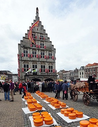 Gouda Cheese Maket. Tall building with crow-step gables in background, cheese-wheels and people in foreground. in or